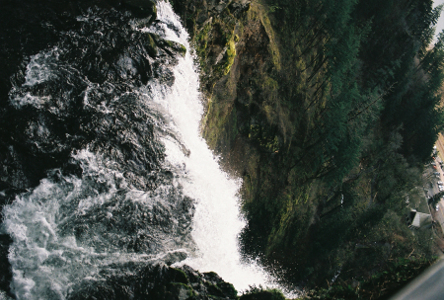 [This view was taken from an overlook directly above the lip of the waterfall so there is some turbulence before the whitewater is created from the drop. Most of the image is hillside covered with trees so the drop is not really evident until one notices the buildings in the lower corner which are at the parking lot level.]